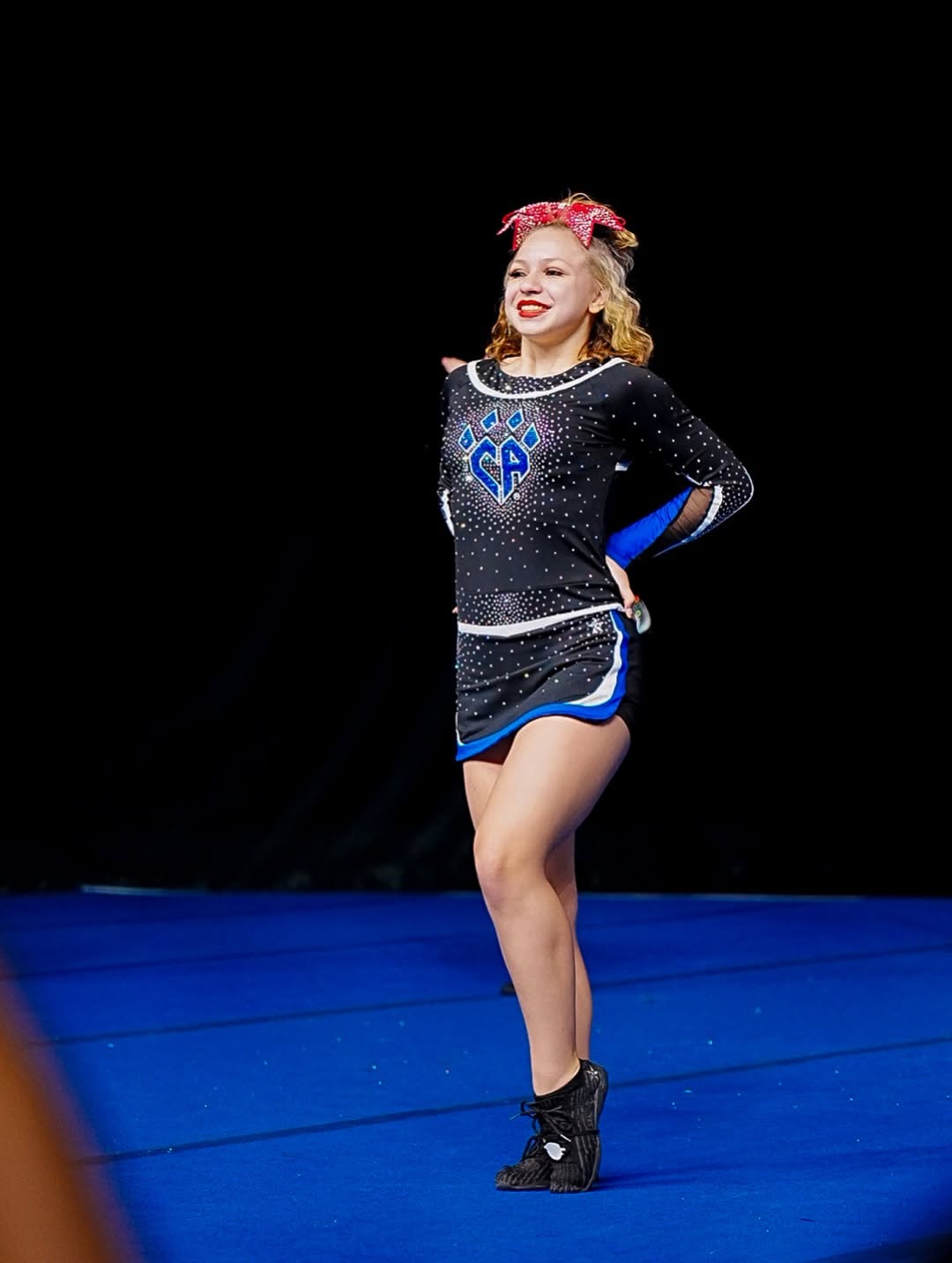 Cheer athlete performing on a blue competition mat, showing confidence, posture, and cheer tumbling readiness.
