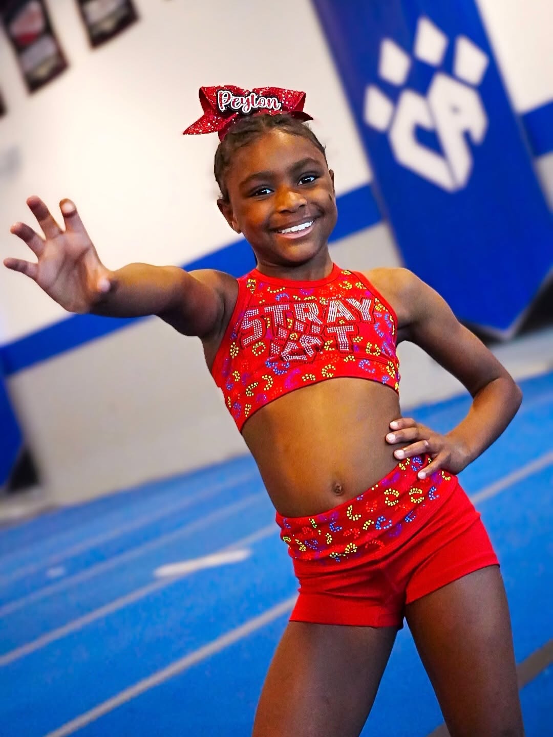 Young cheer athlete smiling on a blue tumbling mat during kids tumbling and cheer training.